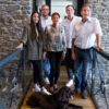 Fünfköpfiges Team des Schulte Bauunternehmens steht lächelnd auf einer Treppe mit Bürohund in modernem Bürogebäude