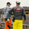 Zwei Bauarbeiter von Schulte Bauunternehmen in Arbeitskleidung bei der Besprechung auf einer Baustelle